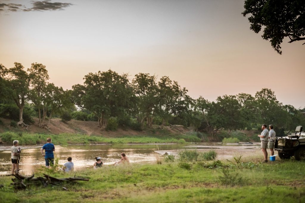 Safari guides and travellers stood on a grass bank looking out to the water