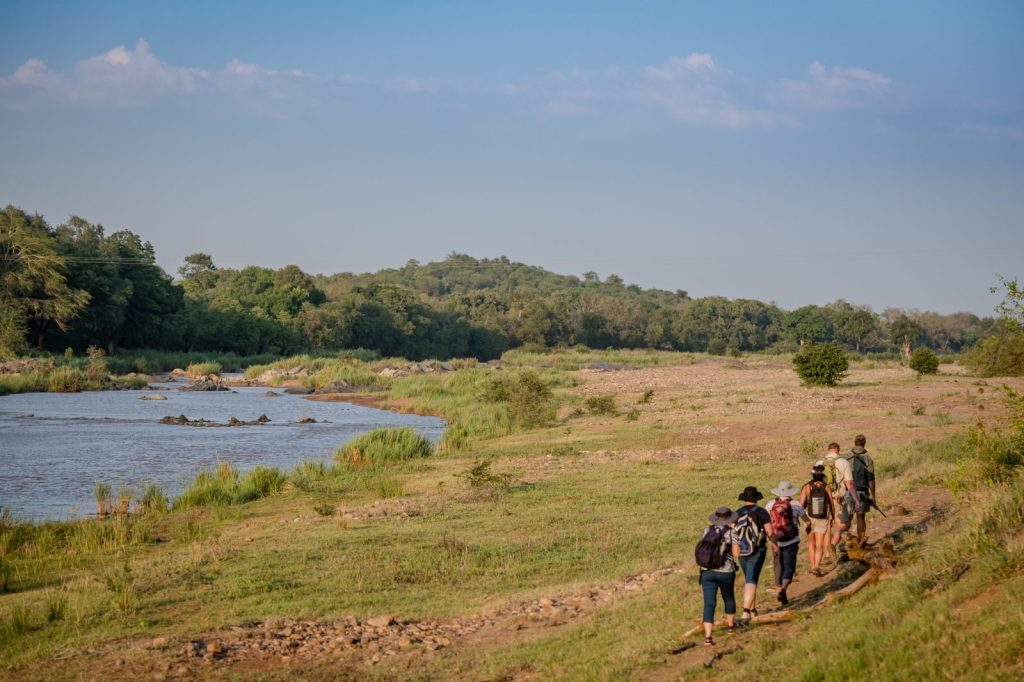 Landscape shot of 6 people with backpacks walking along a path in dry land