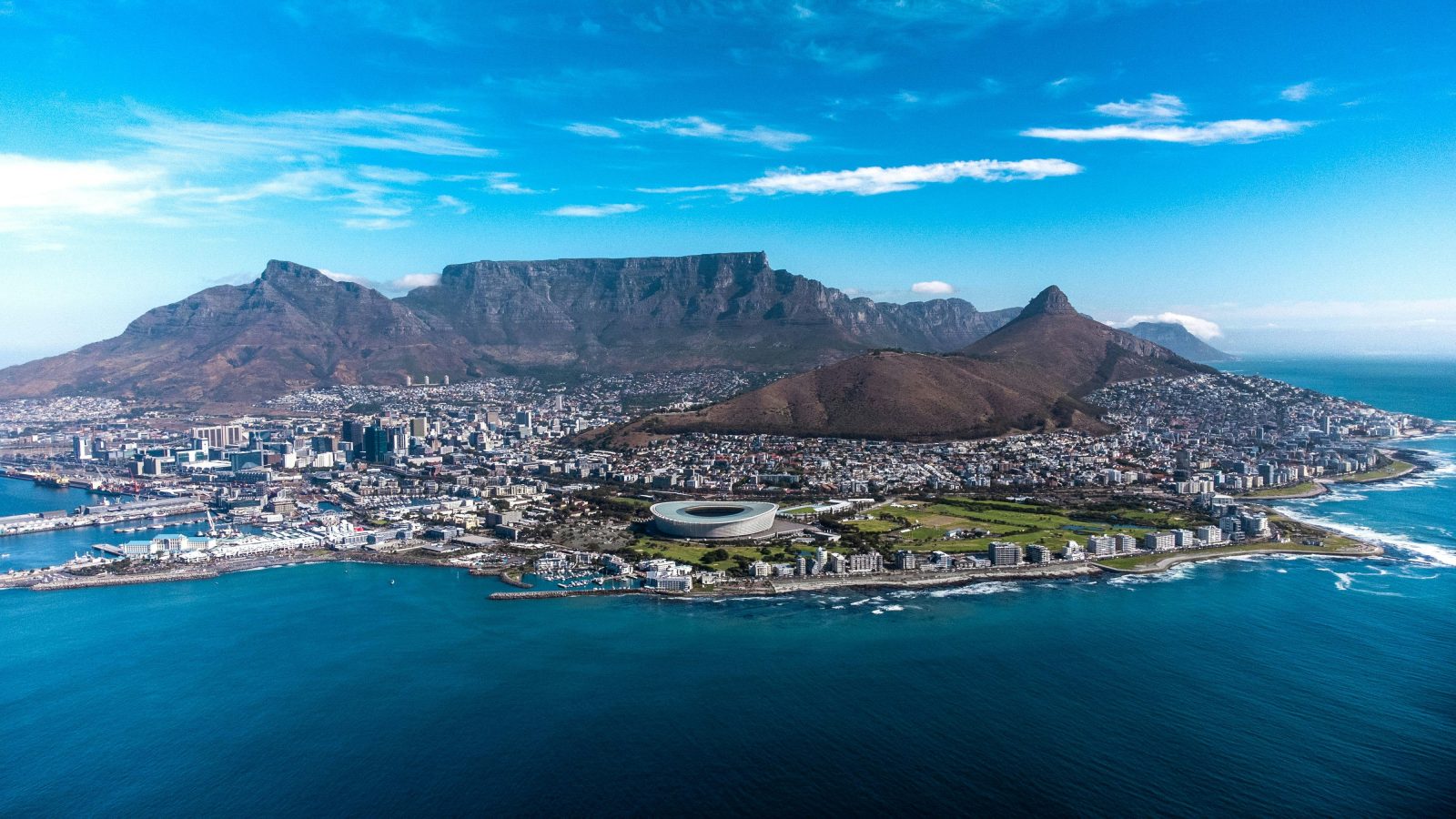 Landscape shot of Cape Town - a built up city with high rise buildings surrounded by the sea with mountains in the background